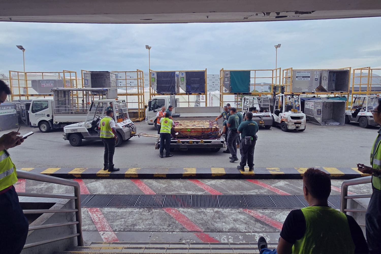 Airport ground crew and officials gather around a large crate on a cargo cart on the tarmac.